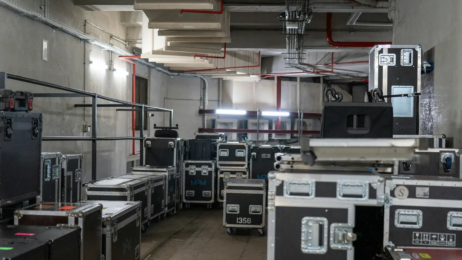 Flight cases noirs et rouges de matériel scénique empilés dans un couloir de stockage en béton
