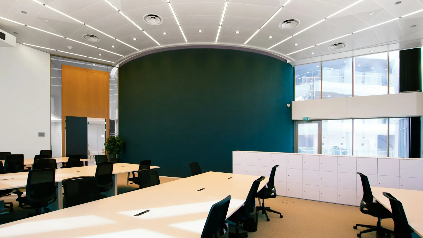 Salle de réunion vide : tables blanches en îlots et fauteuils noirs face à un mur bleu sombre