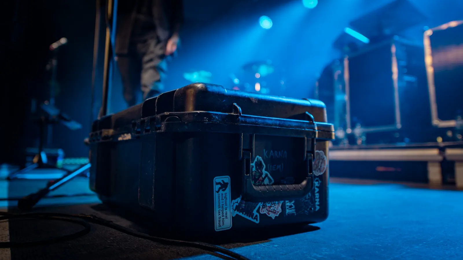 Black equipment case on a stage lit in blue, with amplifiers and stage gear behind it