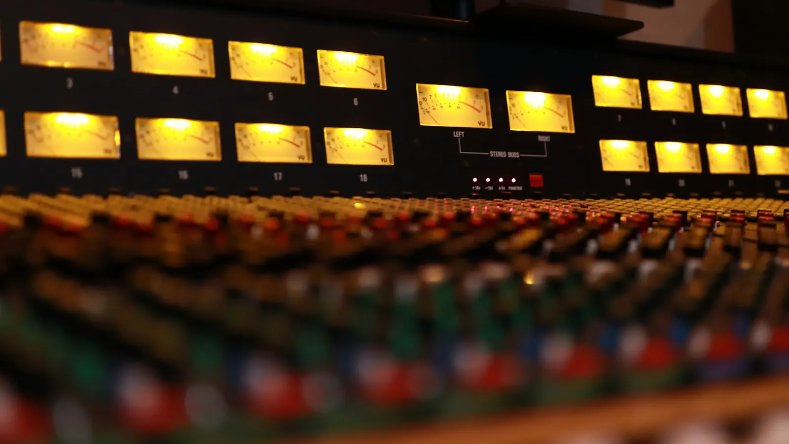 Gros plan sur une console de mixage analogique avec ses vumètres éclairés et ses rangées de potentiomètres