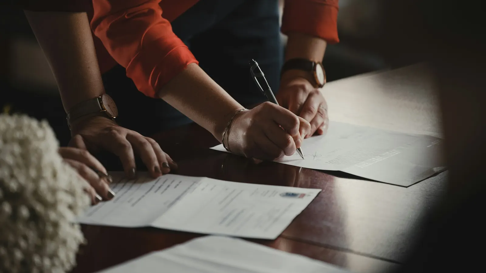 Des mains sur une table : l'une signe un document, d'autres tiennent des feuilles