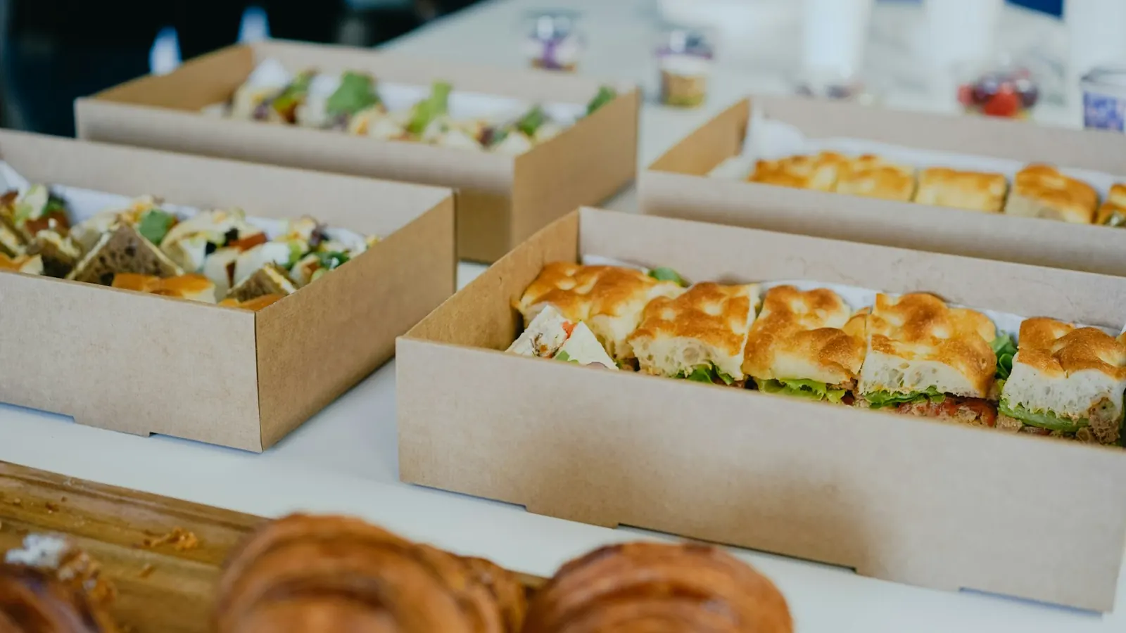 Boîtes en carton de sandwichs et viennoiseries alignées sur une table de buffet