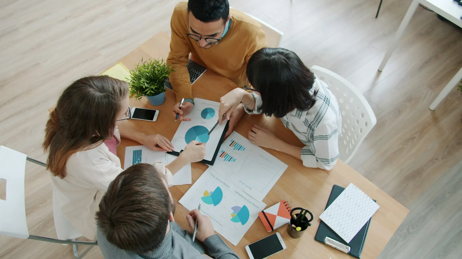 Three colleagues seen from above pointing at charts on paper around a shared table