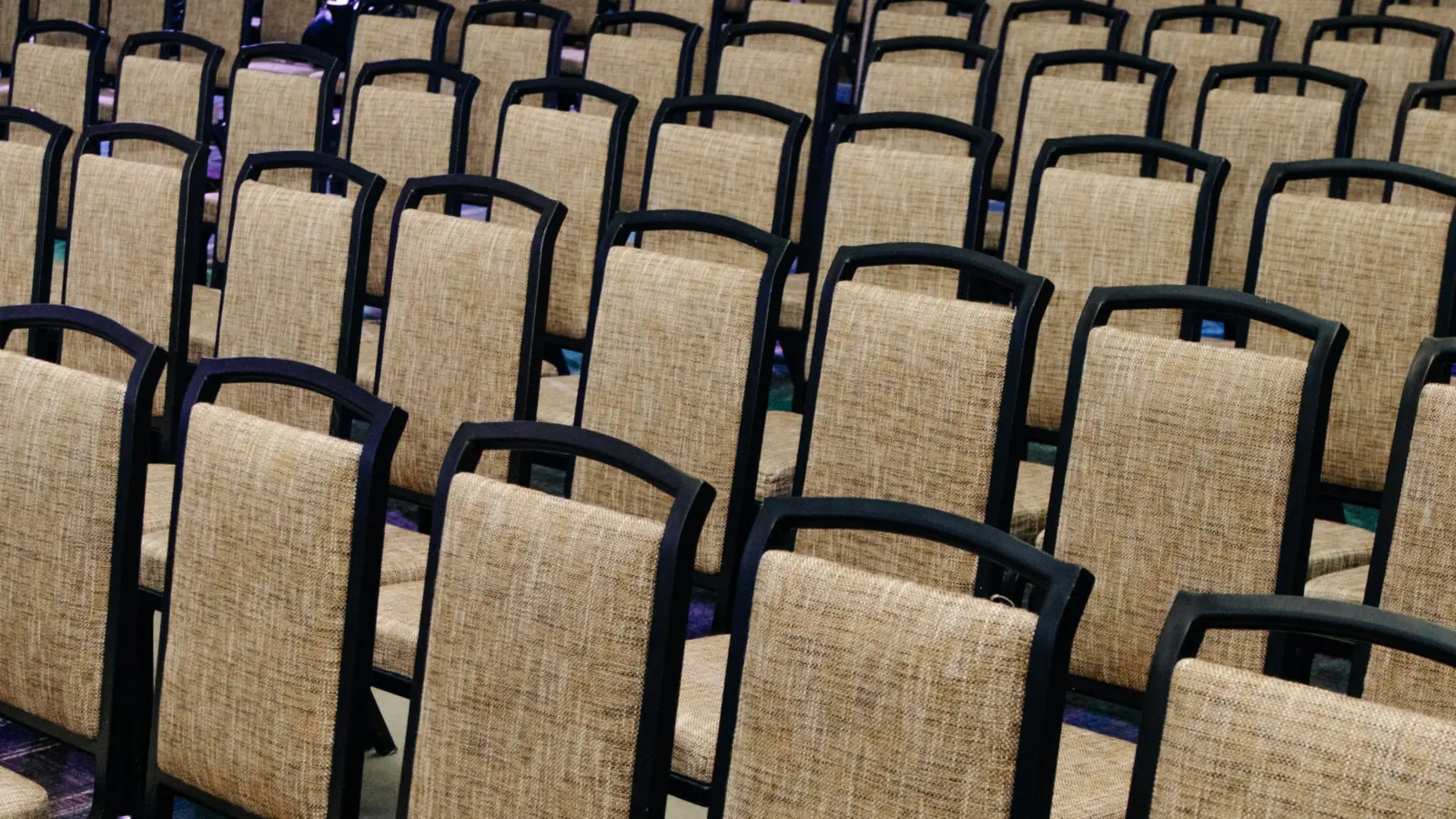 Rows of empty upholstered chairs with black frames, set theater-style in a large hall