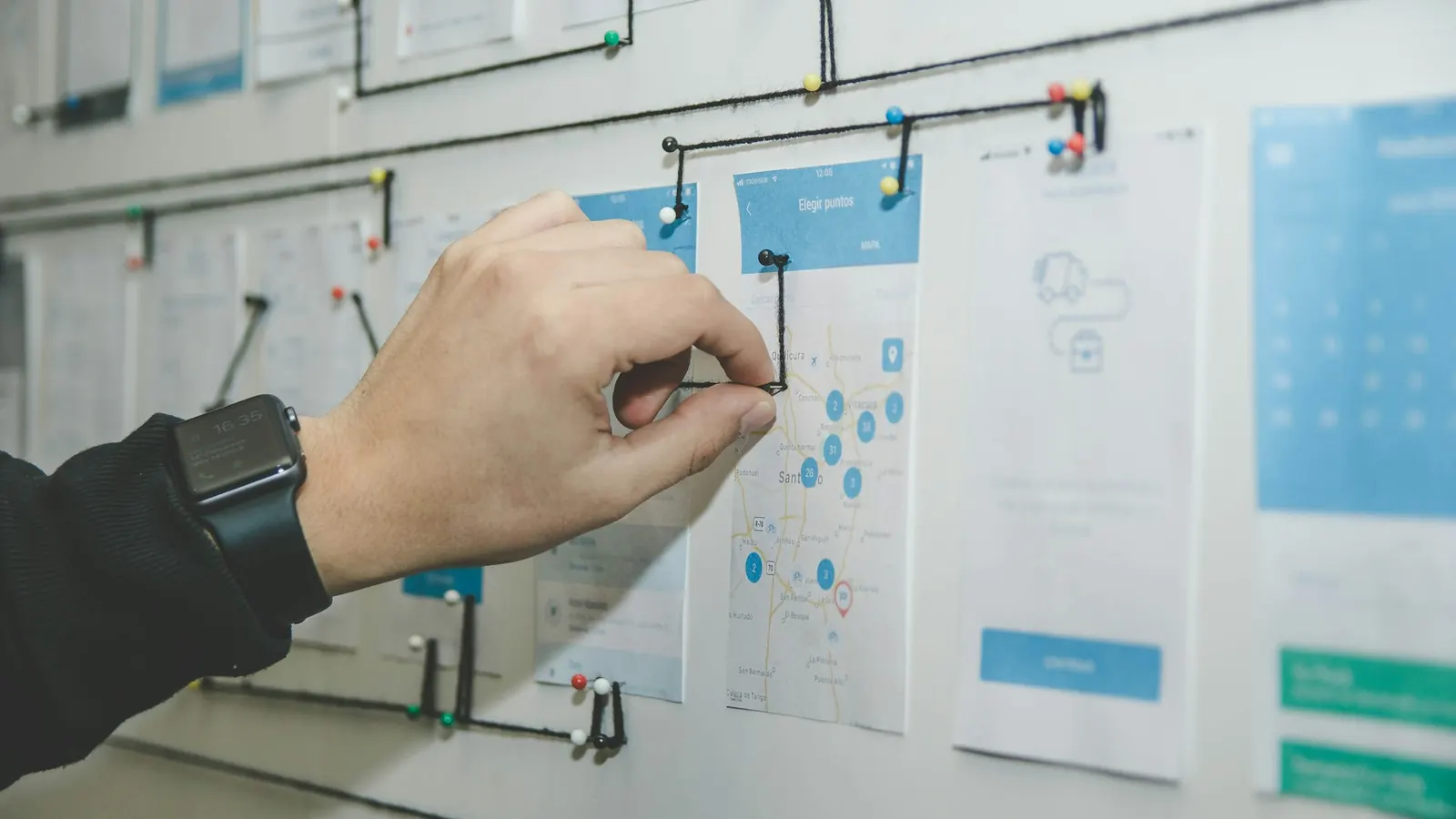 Une main relie au mur, par un fil, des fiches épinglées étape par étape